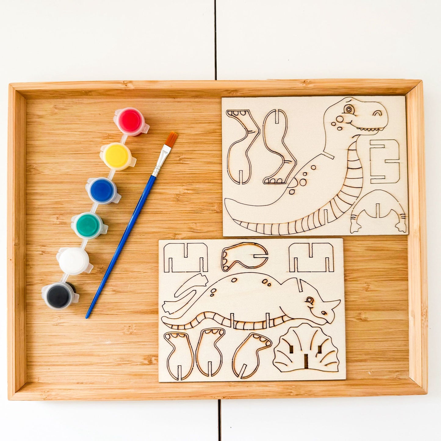 Wooden tray with dinosaur-themed coloring sheets, paint, and brush 