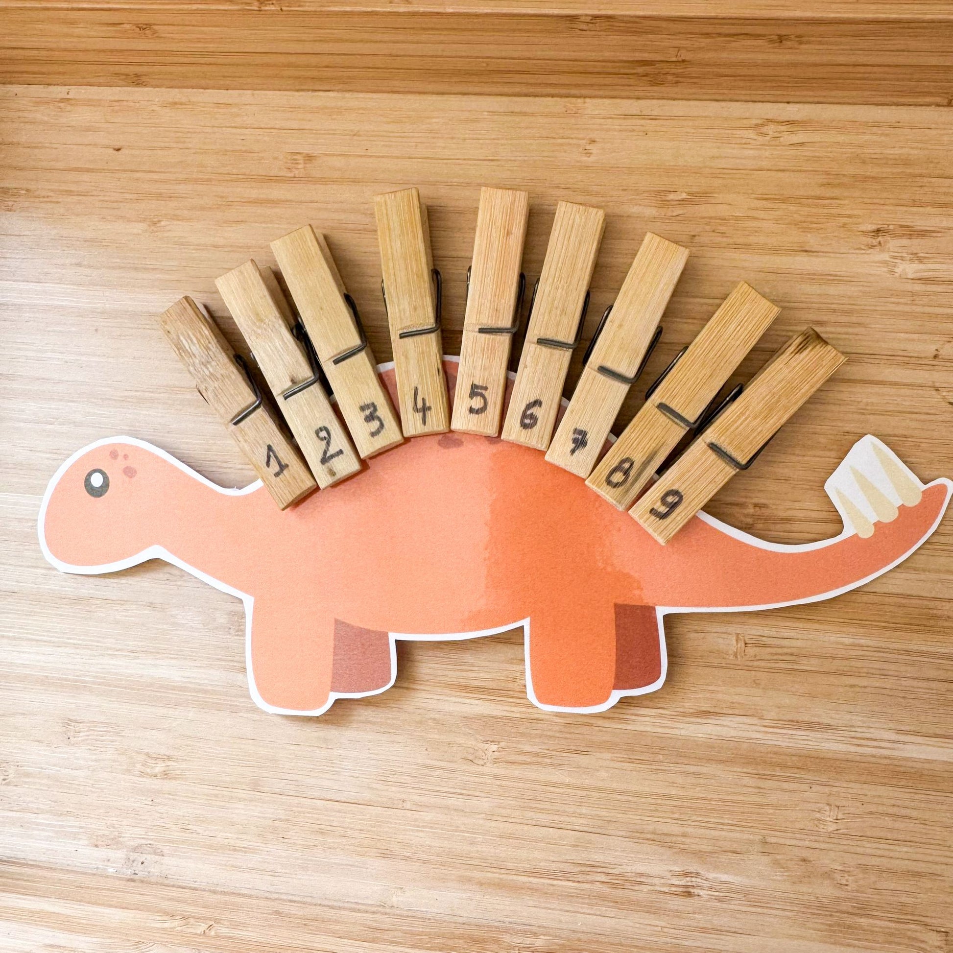 Dinosaur-shaped card with numbered clothespins on a wooden surface