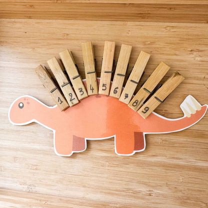 Dinosaur-shaped card with numbered clothespins on a wooden surface