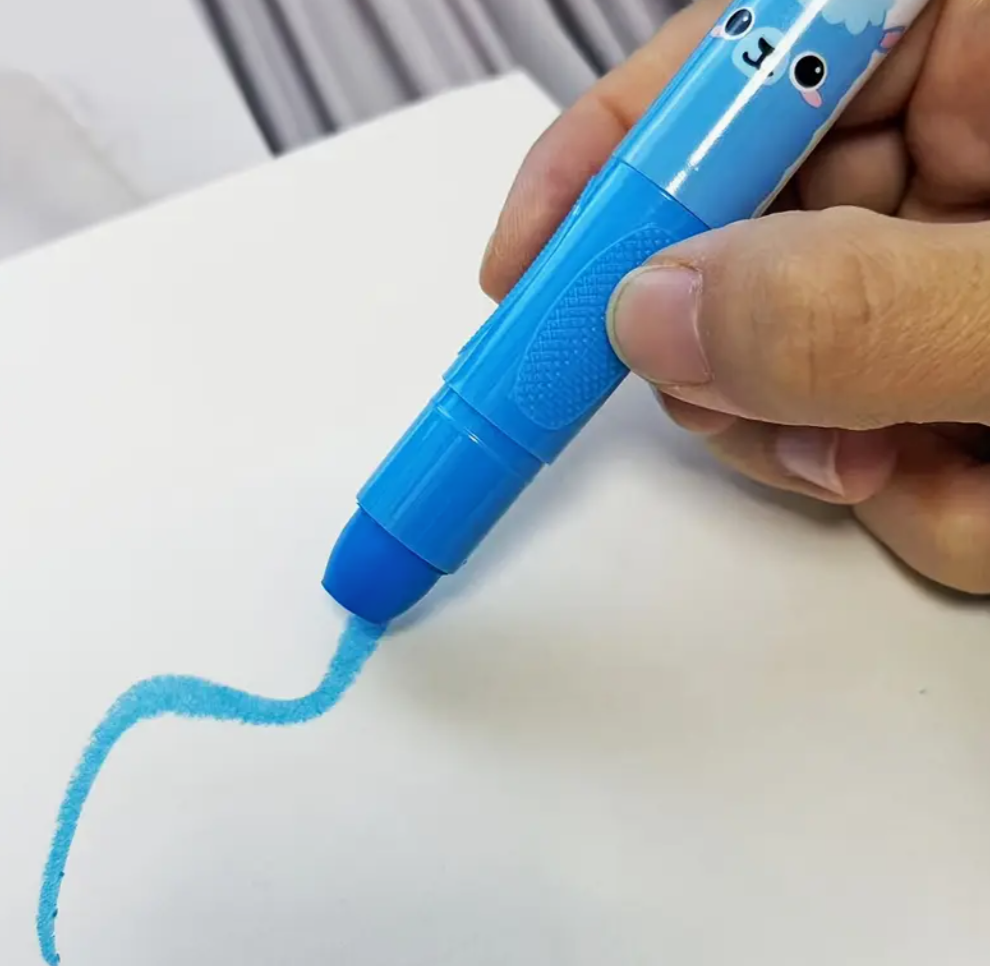 Hand holding a blue pen with a cartoon character on top, drawing on white paper.