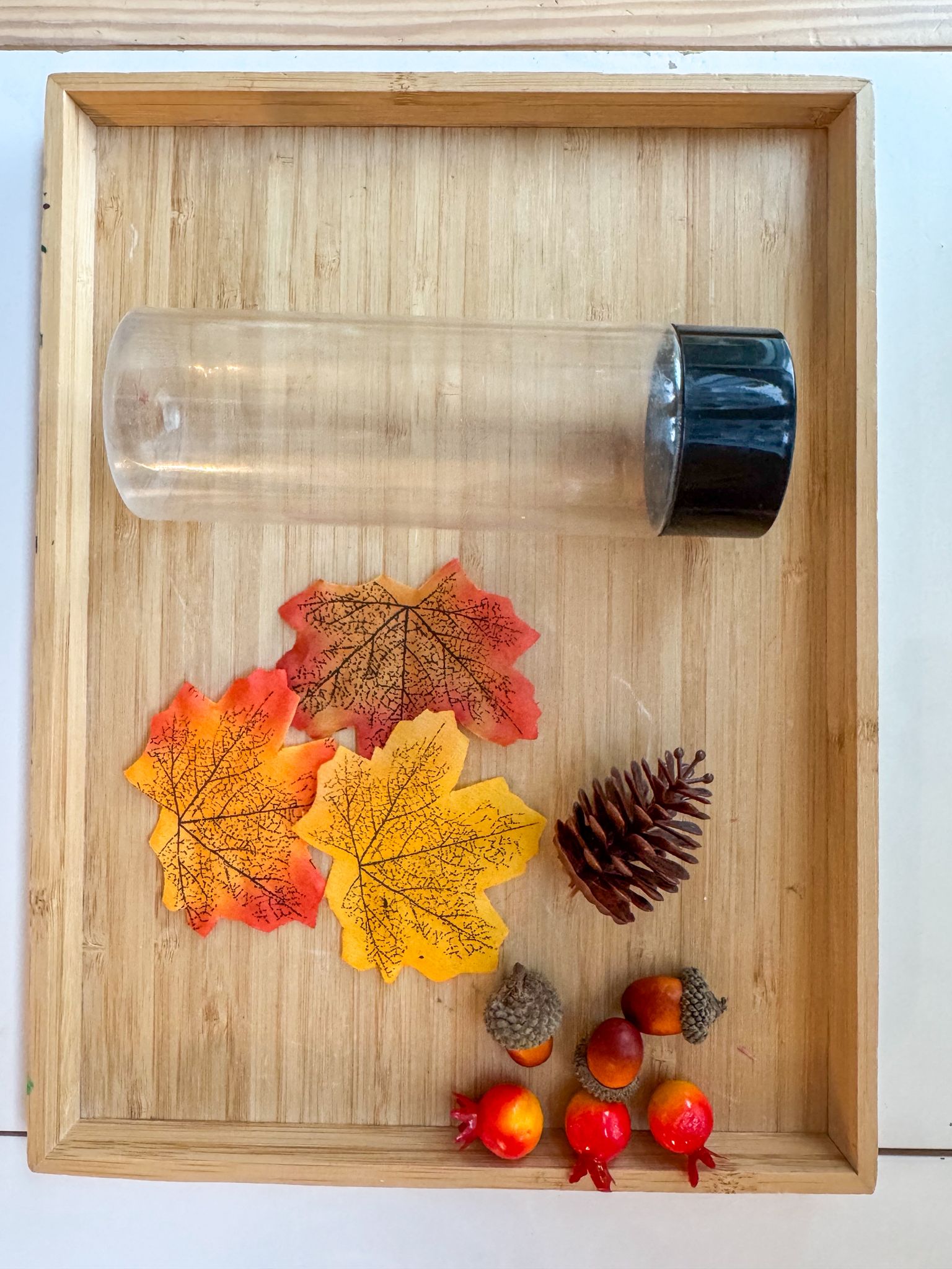 Clear glass tumbler with black lid on a wooden tray with autumn-themed decorations.