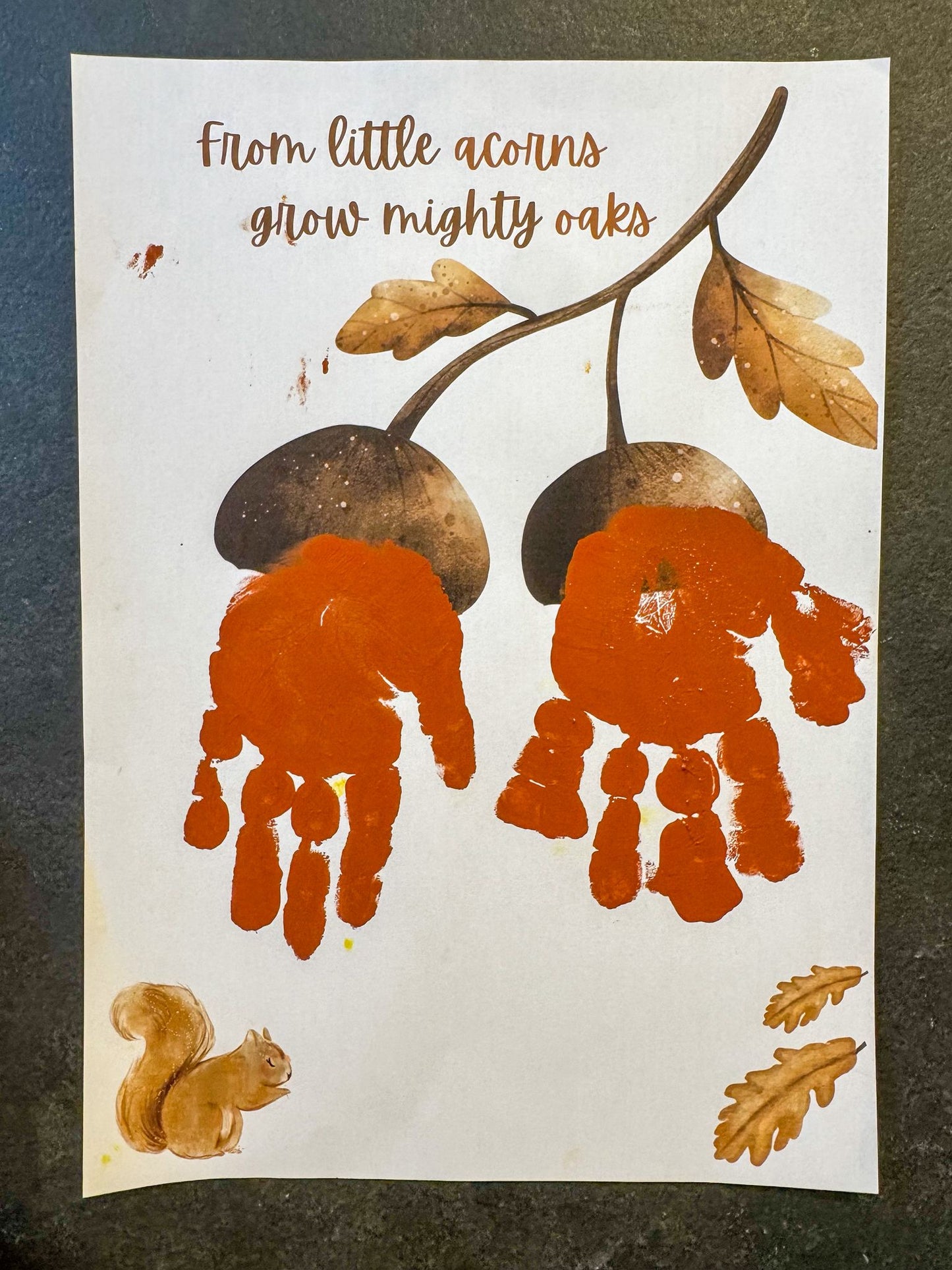 Handprint art with acorns and a squirrel on a white background, featuring the text 'From little acorns grow mighty oaks'.